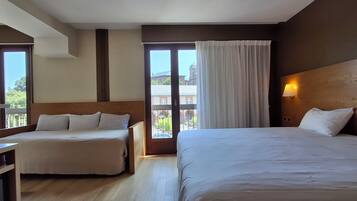 Habitación de hotel con dos camas, cabecera de madera, mesita de noche, ventana con cortinas y vista a edificios.