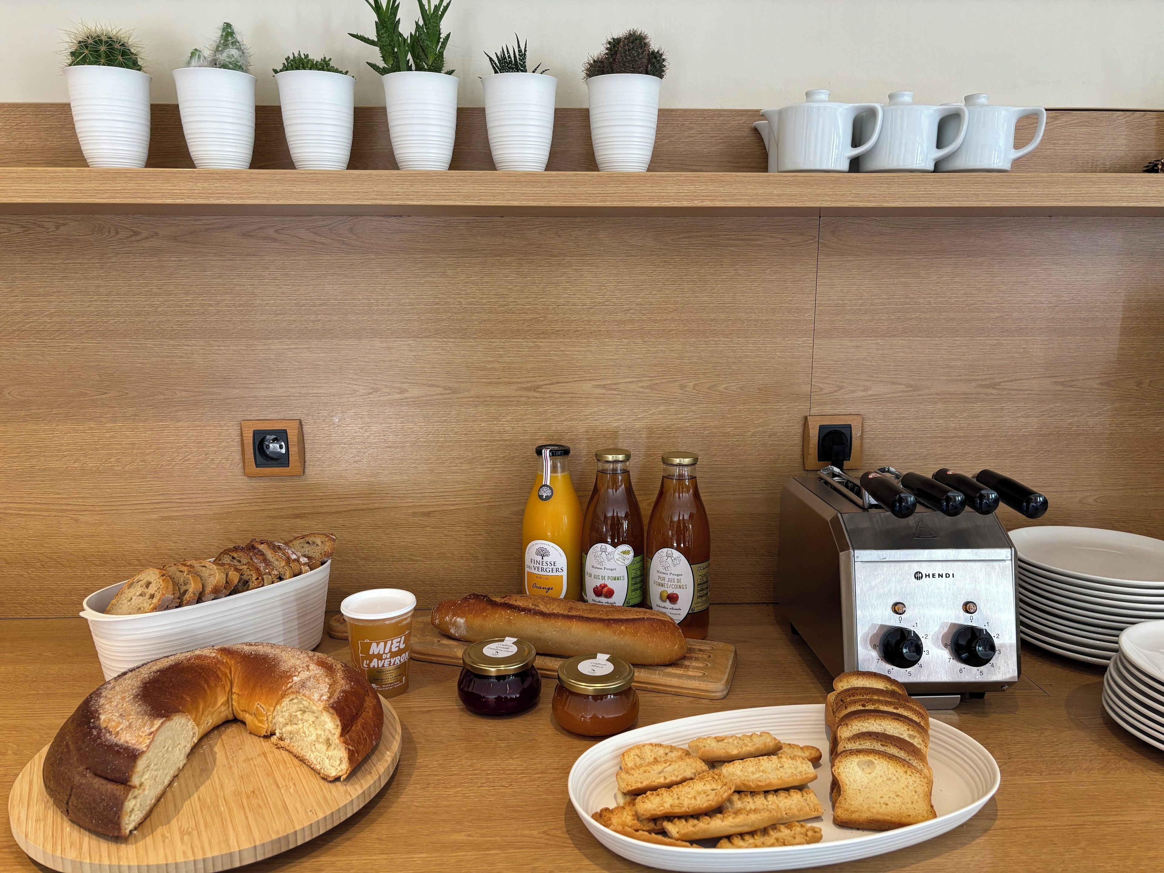 Un bufé de desayuno con pan, bollería, mermeladas y botellas de zumo.