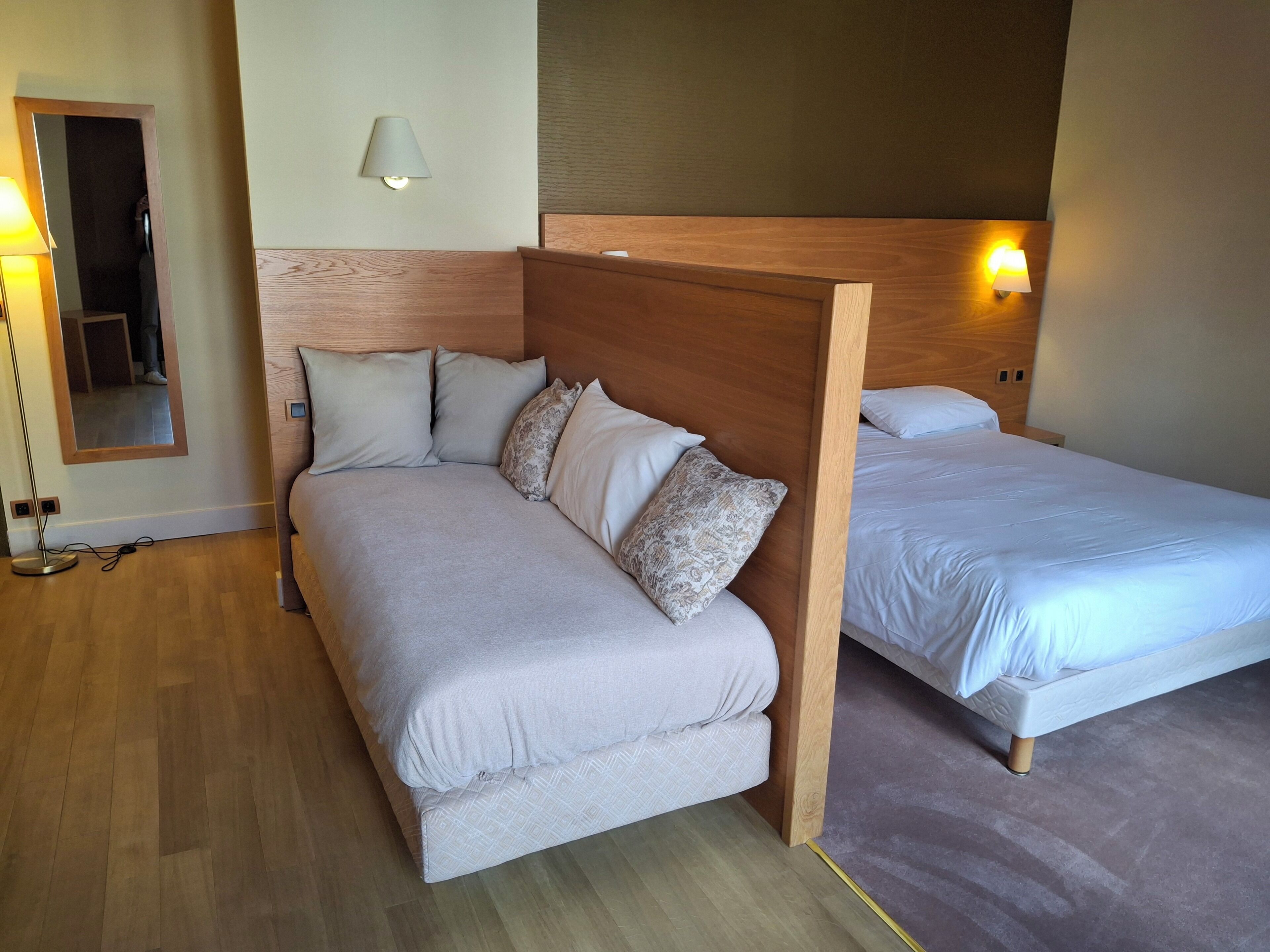 A bedroom with a wooden headboard, a sofa, a single bed, and a bedside lamp.