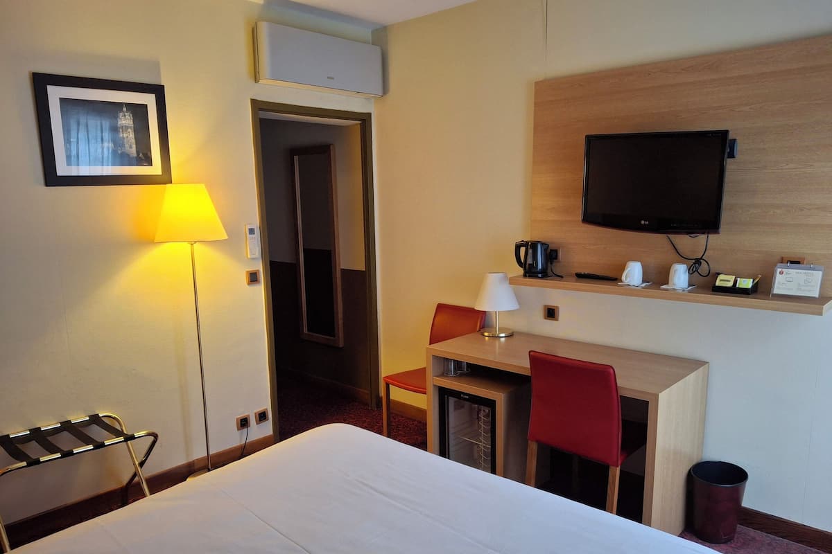 A hotel room with a bed, a desk with a chair, a TV, and a lamp.