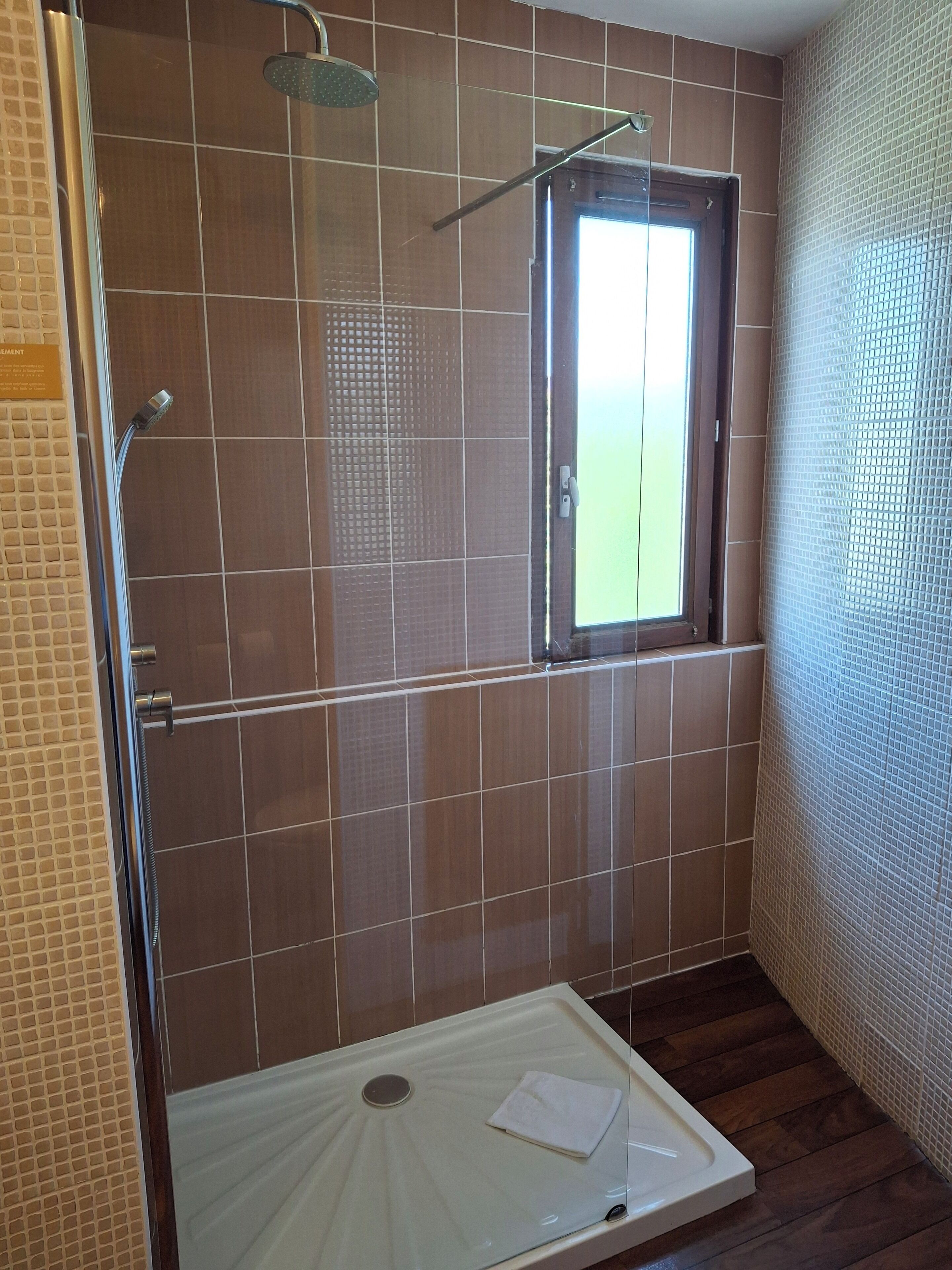 A shower area with a glass door, a window, and a white sink.