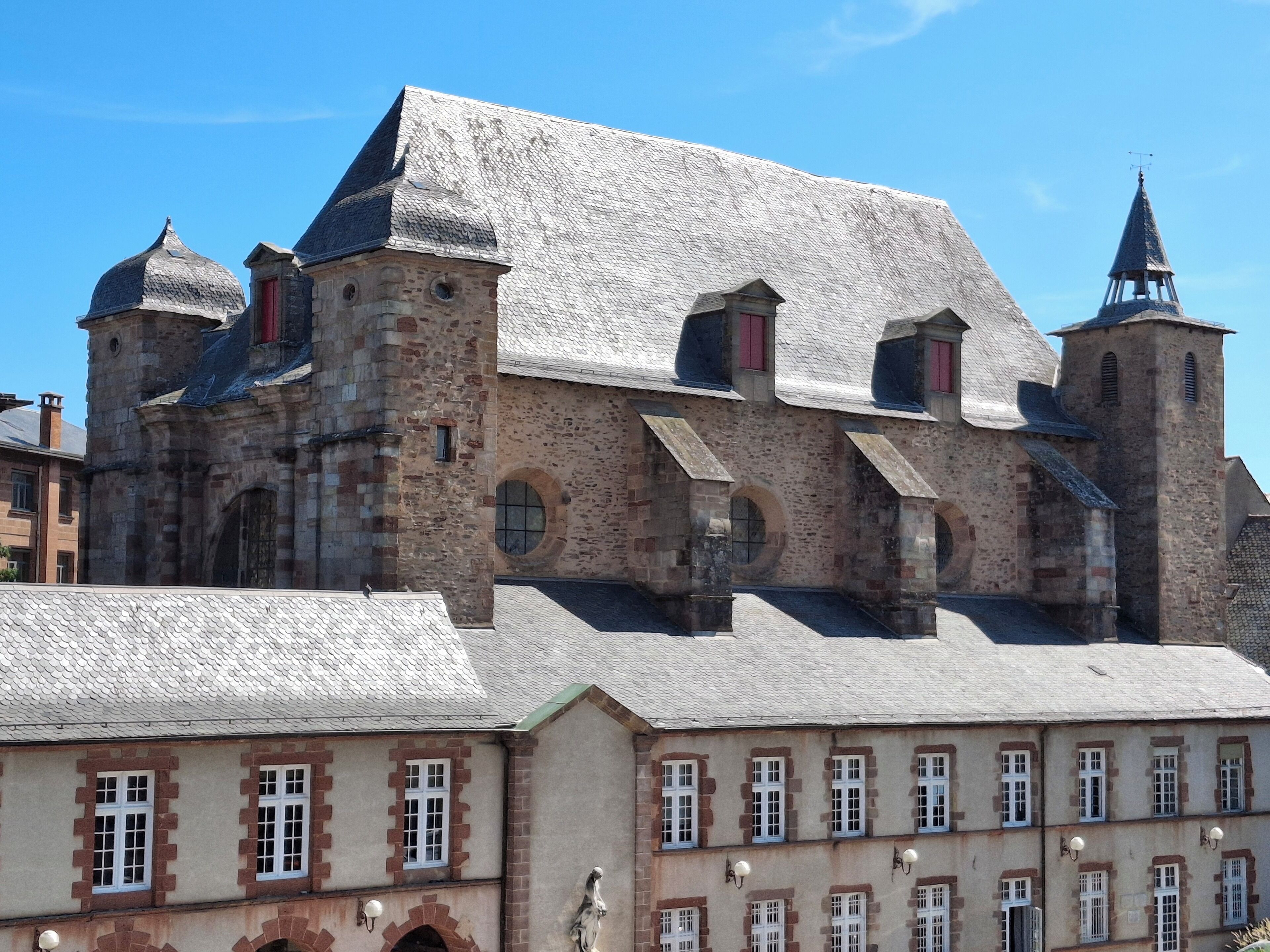 Un bâtiment historique doté de nombreuses tours et de fenêtres en arc de cercle, caractérisé par une façade en pierre et un toit recouvert de tuiles.
