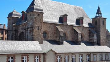 Un bâtiment historique doté de nombreuses tours et de fenêtres en arc de cercle, caractérisé par une façade en pierre et un toit recouvert de tuiles.
