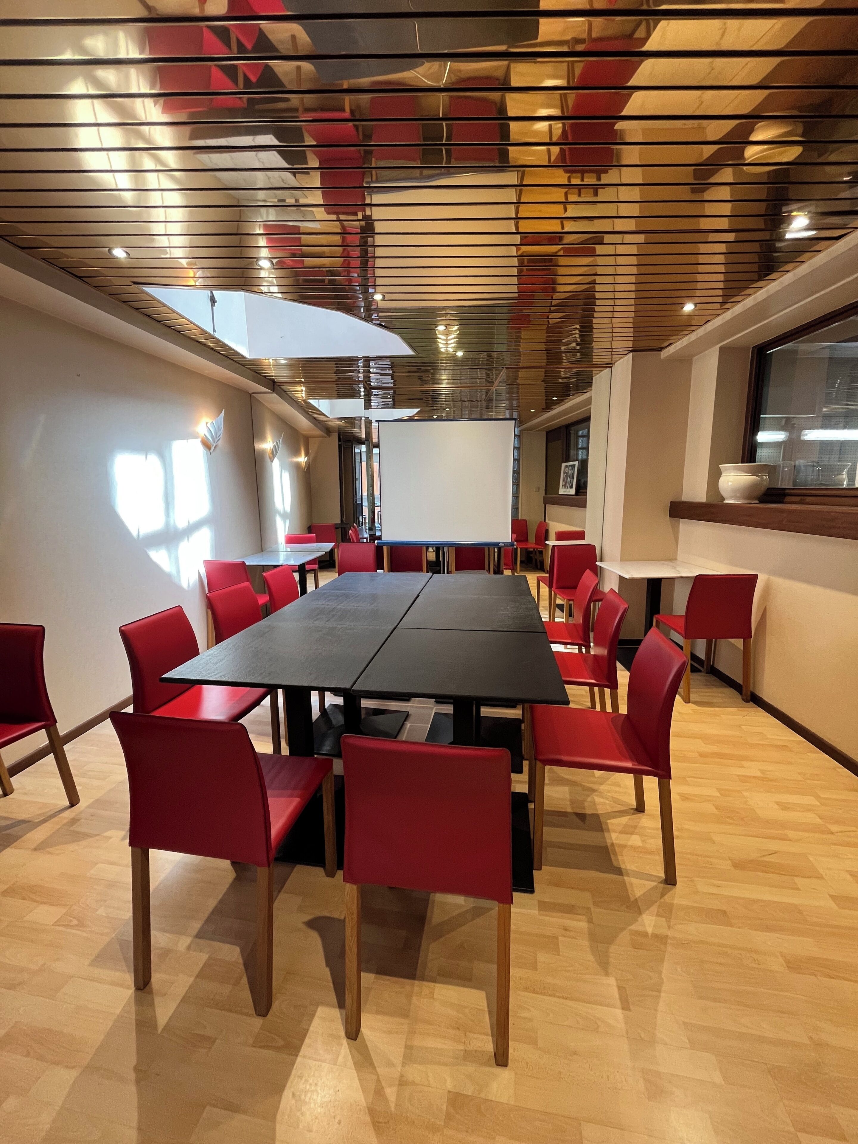 A conference room with a long table and red chairs, a whiteboard, and a window with a view of the city.