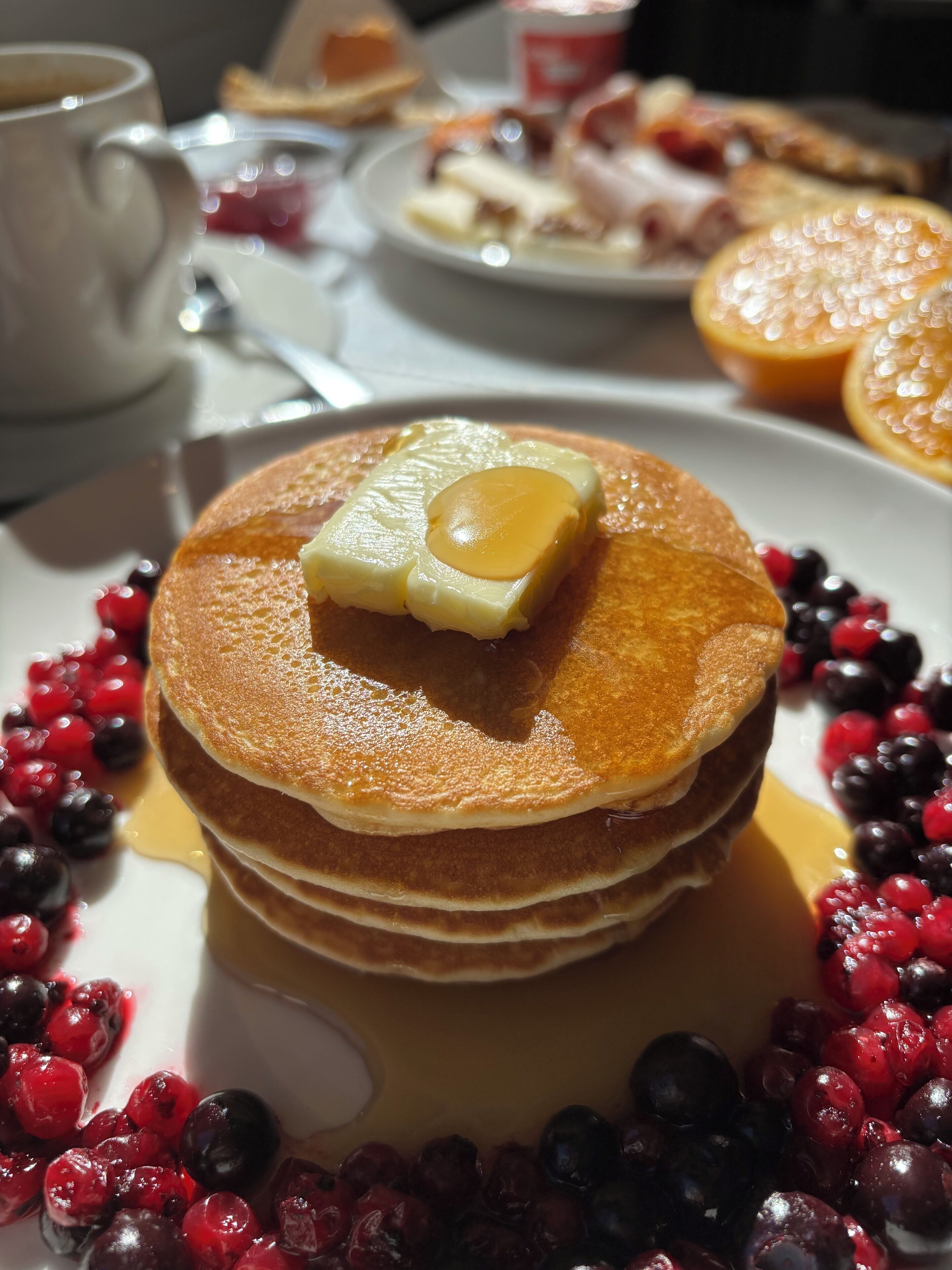 Una pila de panqueques con jarabe y mantequilla, rodeada de bayas.