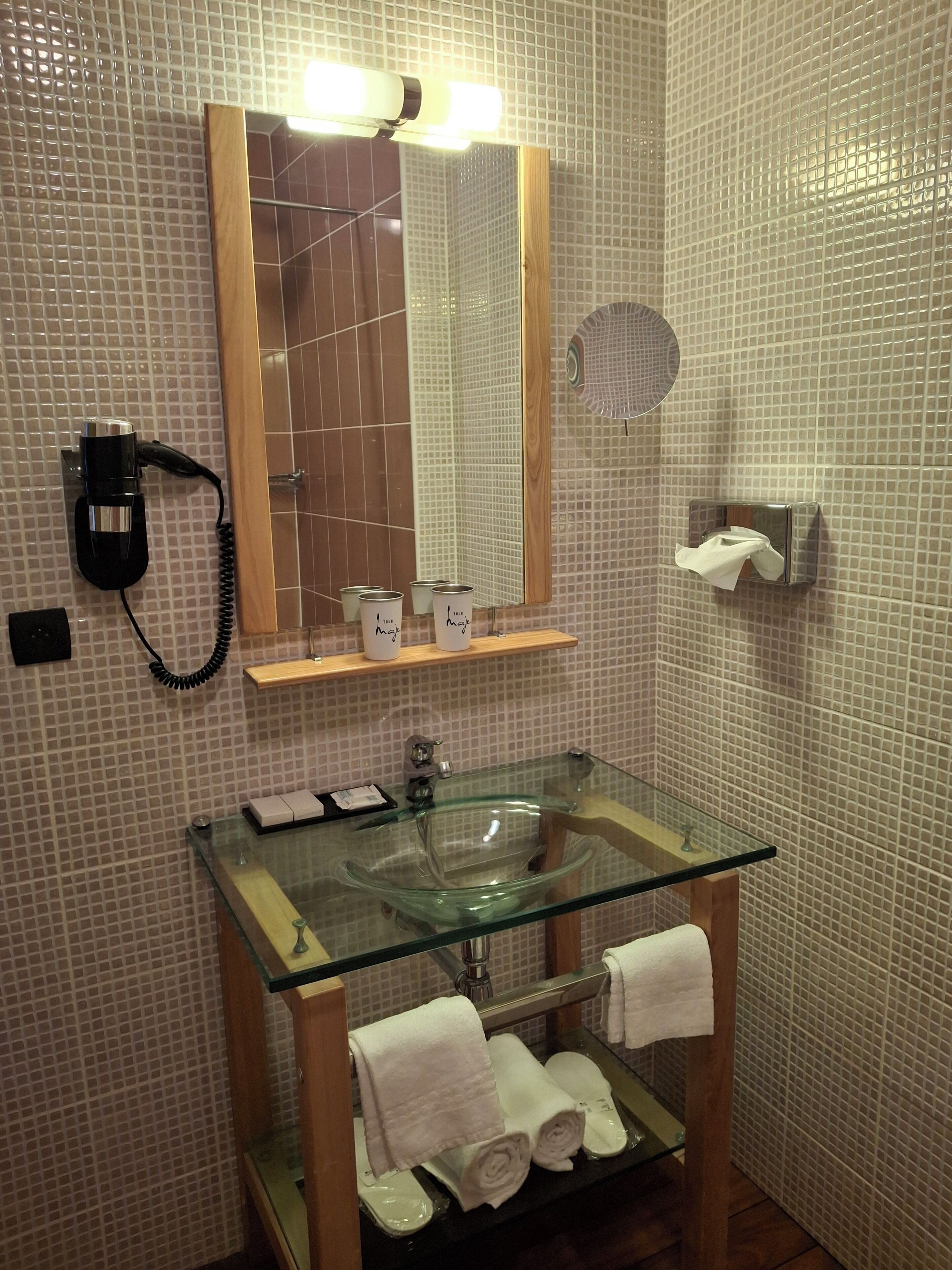 A bathroom with a glass sink, a mirror, a hairdryer, and a towel rack.