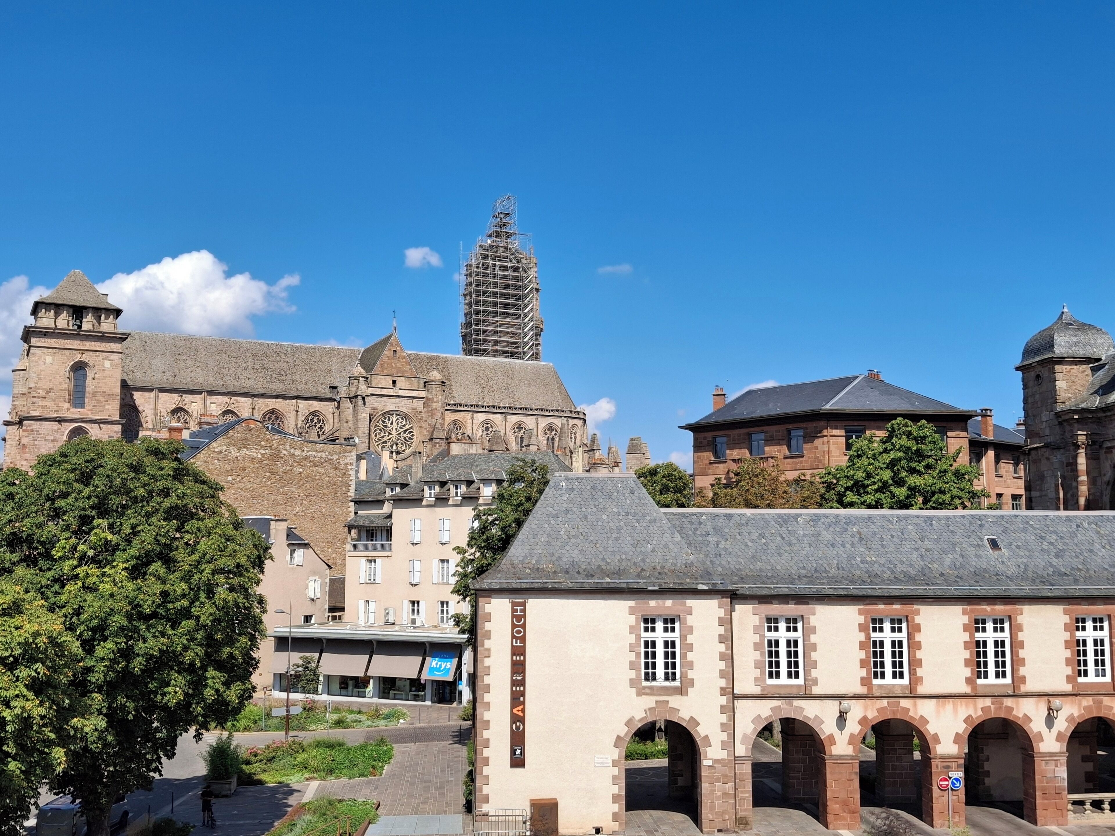A historic building with a prominent tower, a large arched entrance, and a paved courtyard.