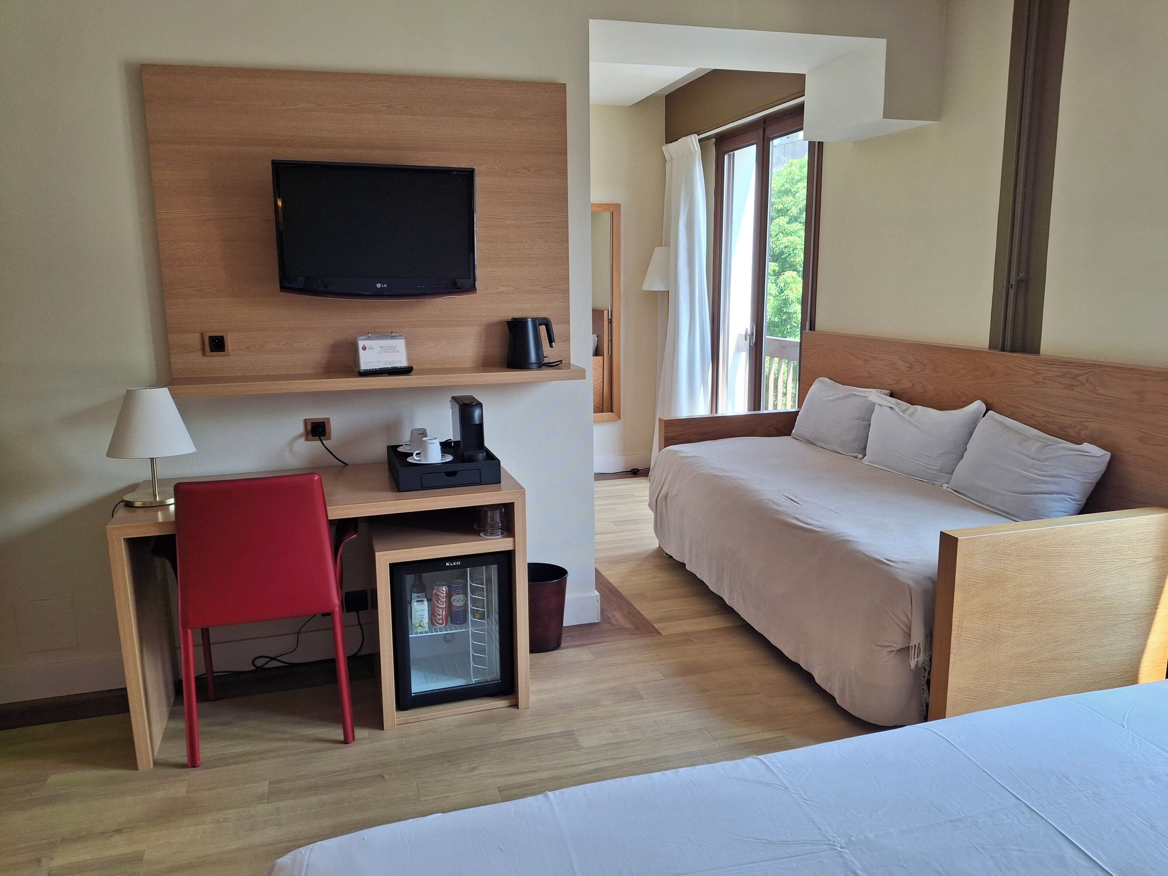Hotelkamer met een bed, bureau met stoel, televisie, koffiezetapparaat en minibar.