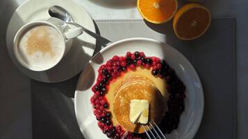 Una mesa de desayuno con platos de comida, incluyendo tostadas, carnes, queso y frutas, además de una taza de café y un vaso de jugo de naranja.