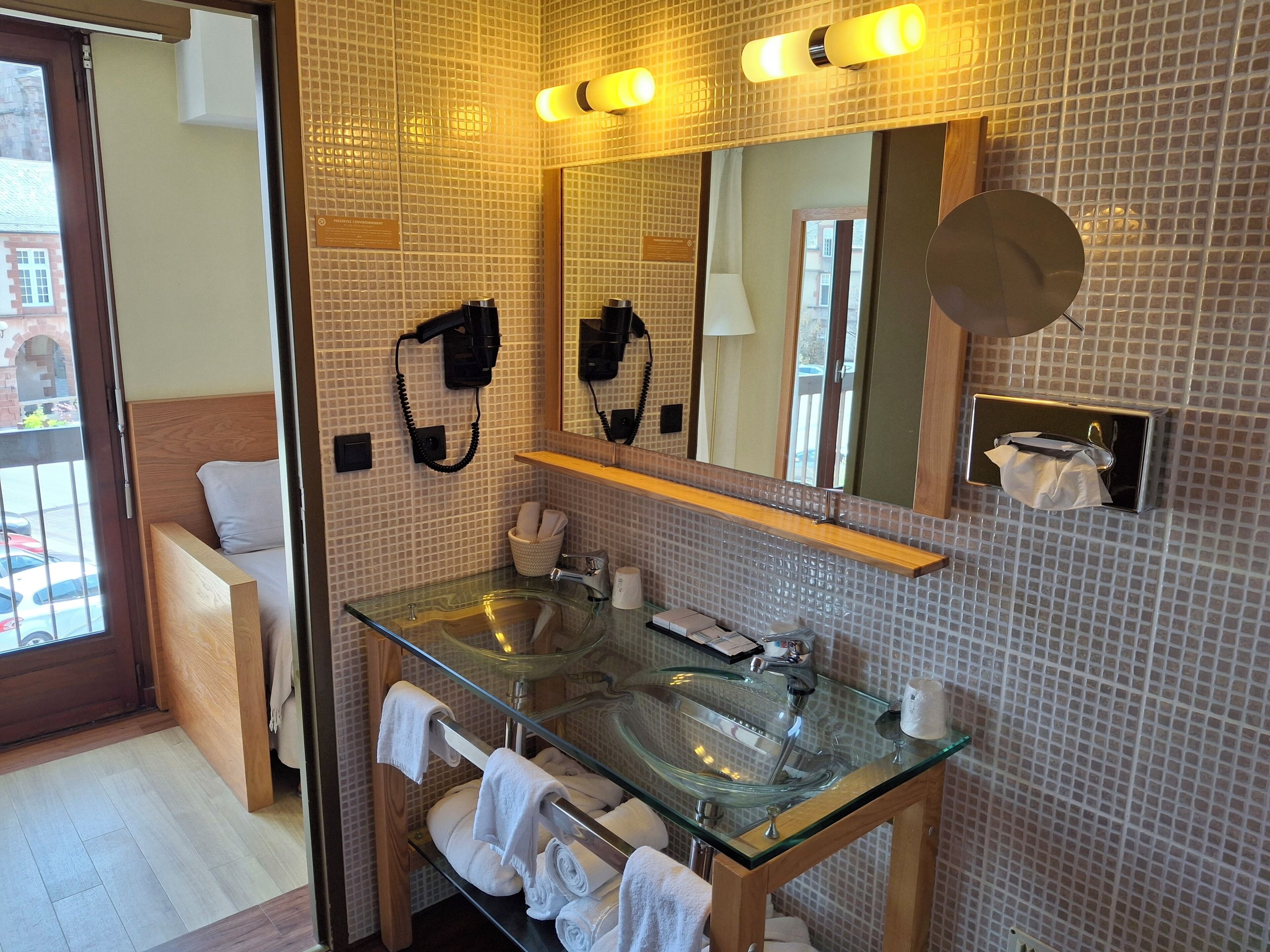 A bathroom with a glass sink, a mirror, a hairdryer, and a towel rack.