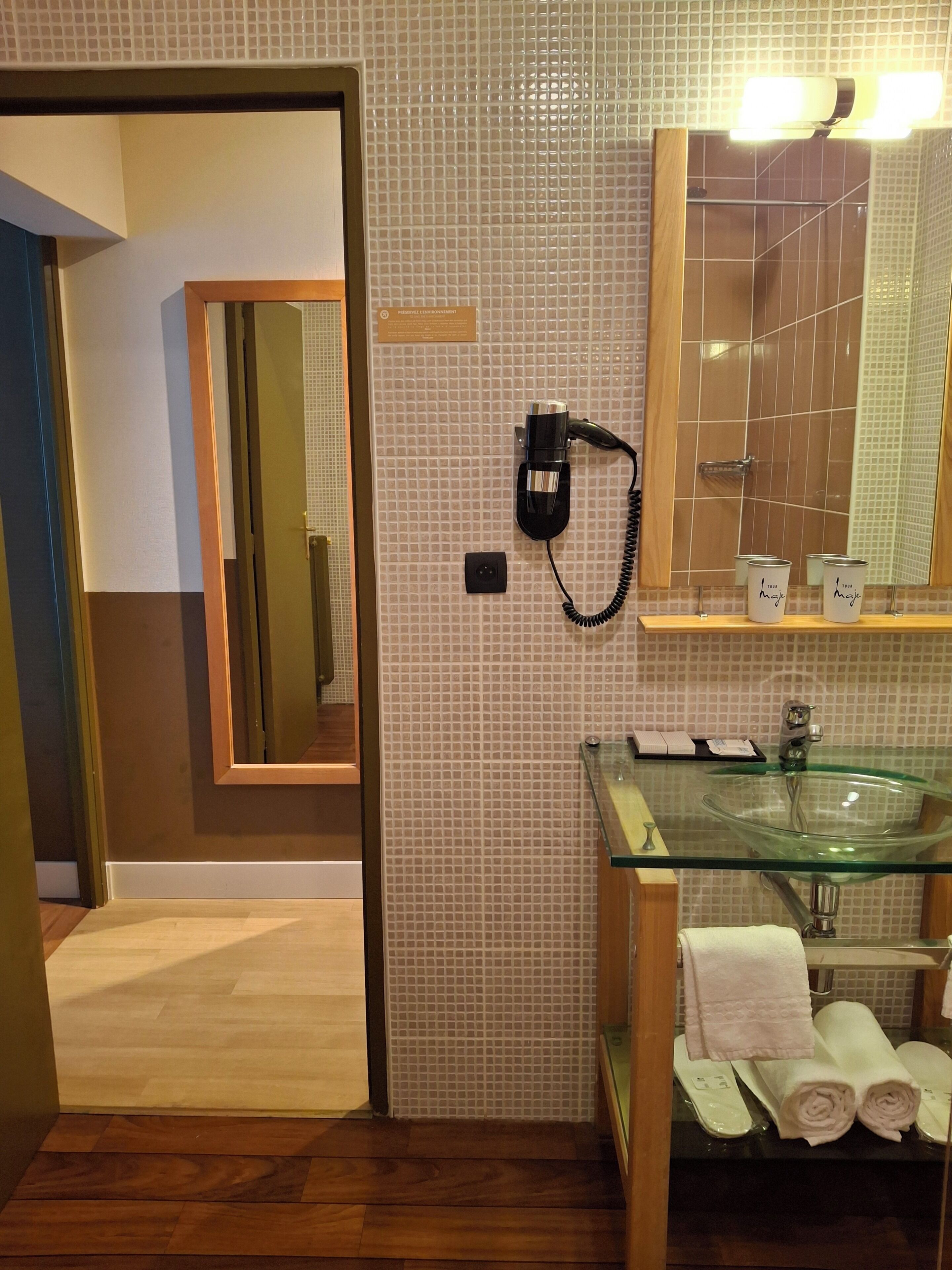 Een hotelbadkamer met een glazen wastafel, een spiegel, een telefoon en handdoeken.