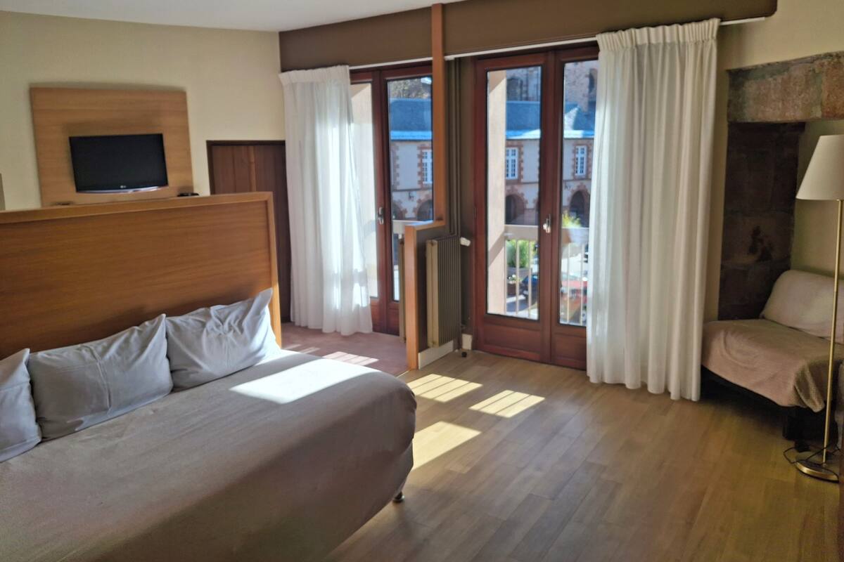A hotel room with a bed, a TV, a lamp, and a view of the outside.