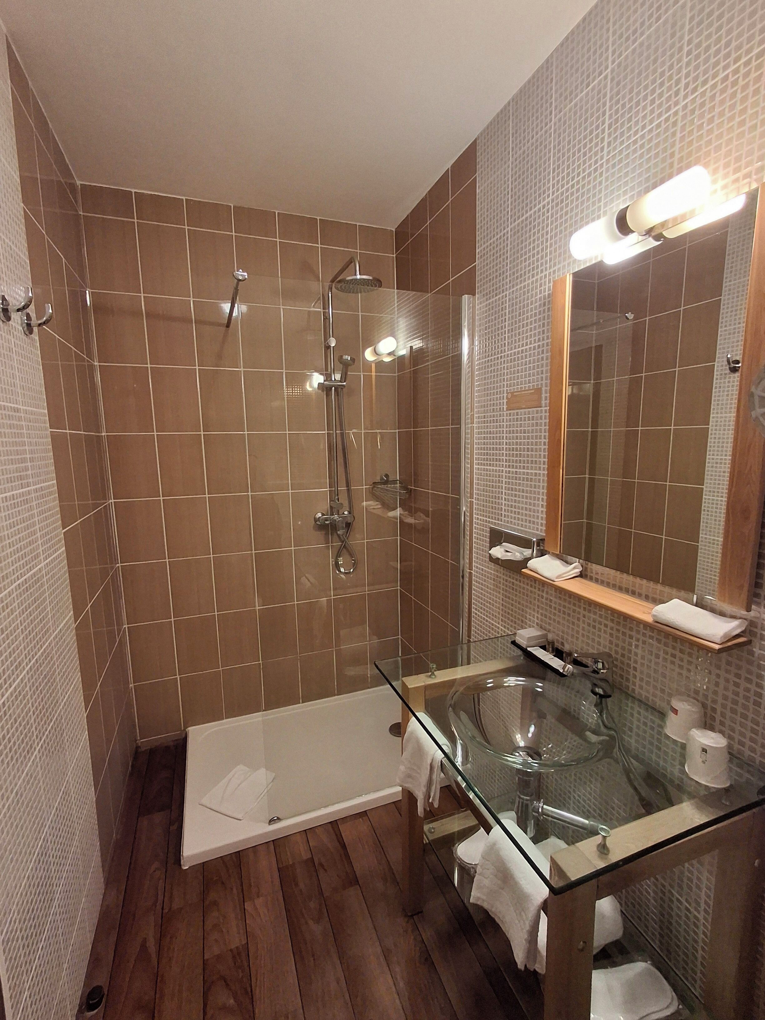 A modern bathroom with a glass-enclosed shower, a glass sink, and a wooden floor.