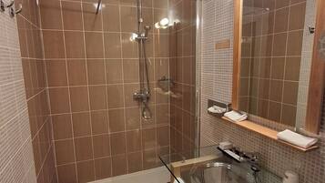 A modern bathroom with a glass-enclosed shower, a glass sink, and a wooden floor.