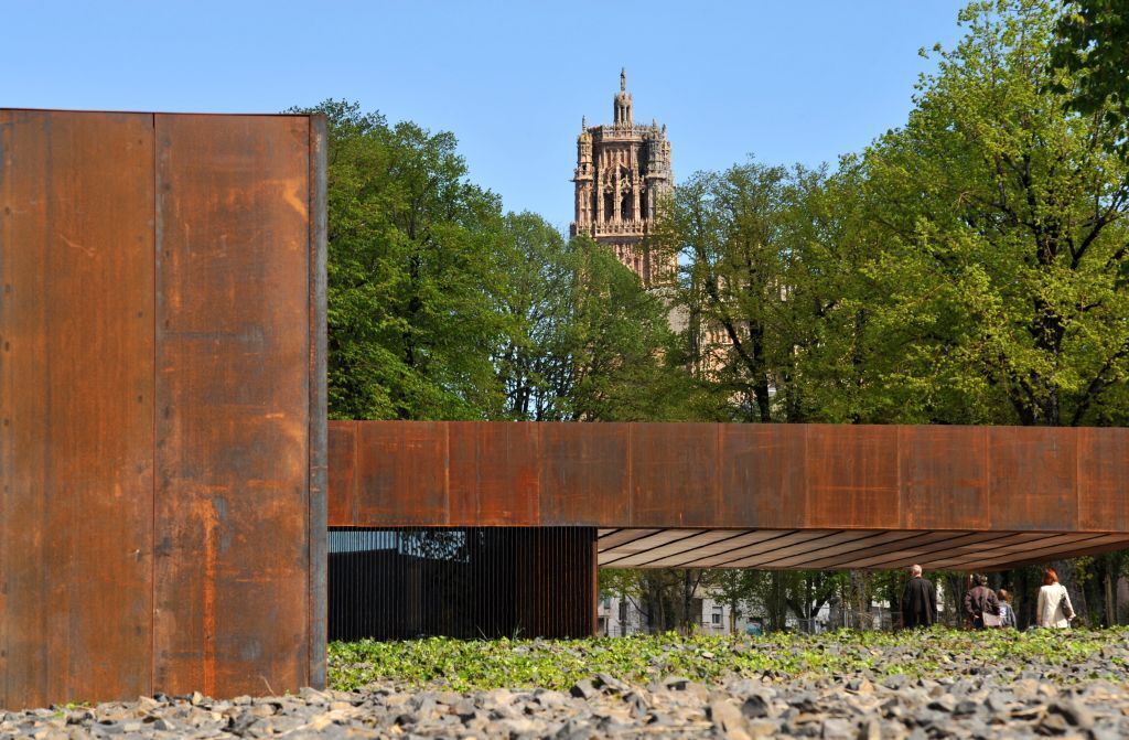 A modern building with a large metal structure in the foreground and a historic tower in the background.