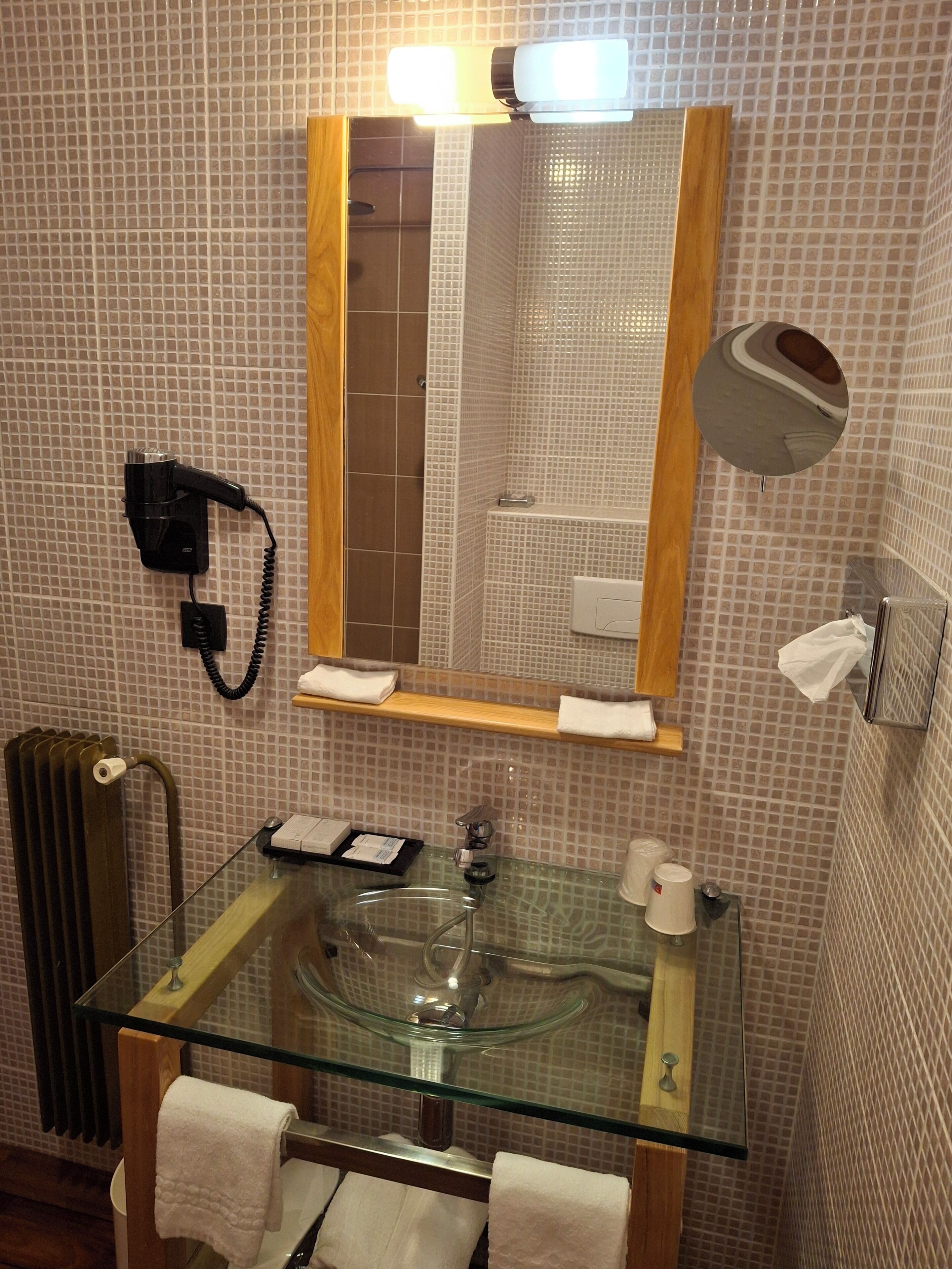 A bathroom with a glass sink, a mirror, a hairdryer, and a towel rack.