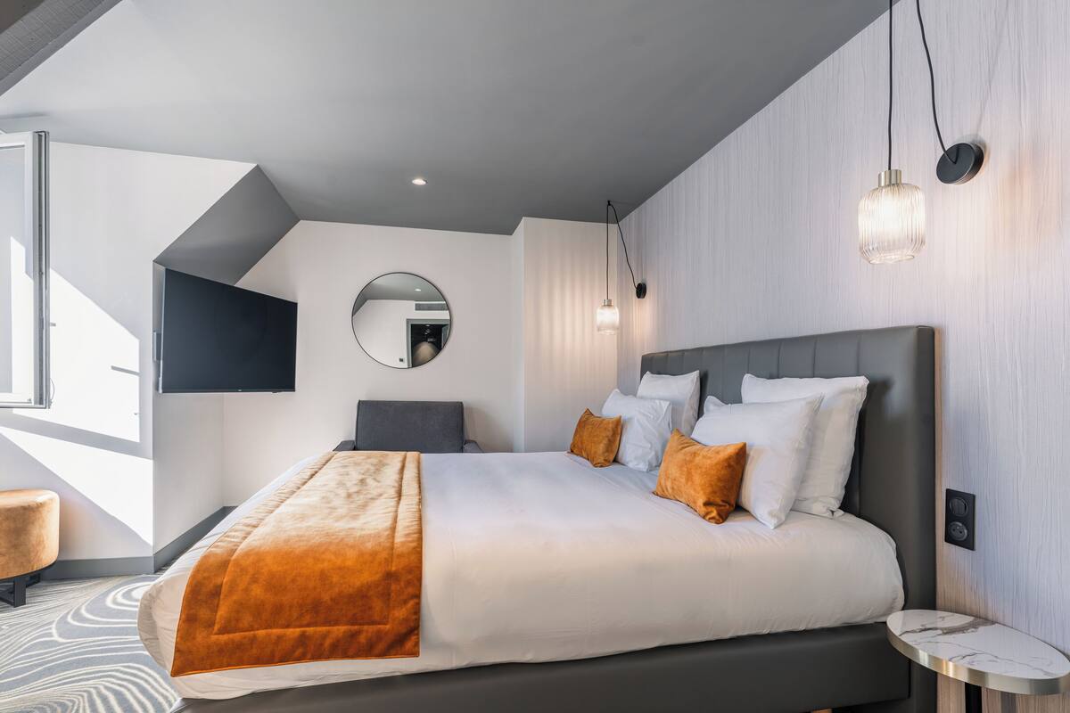A modern hotel room with a large bed, a flat-screen TV, a round mirror, and a small side table.