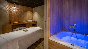 Une salle de spa équipée d’une table de massage, d’un mur en bois et d’un jacuzzi éclairé de lumières bleues.