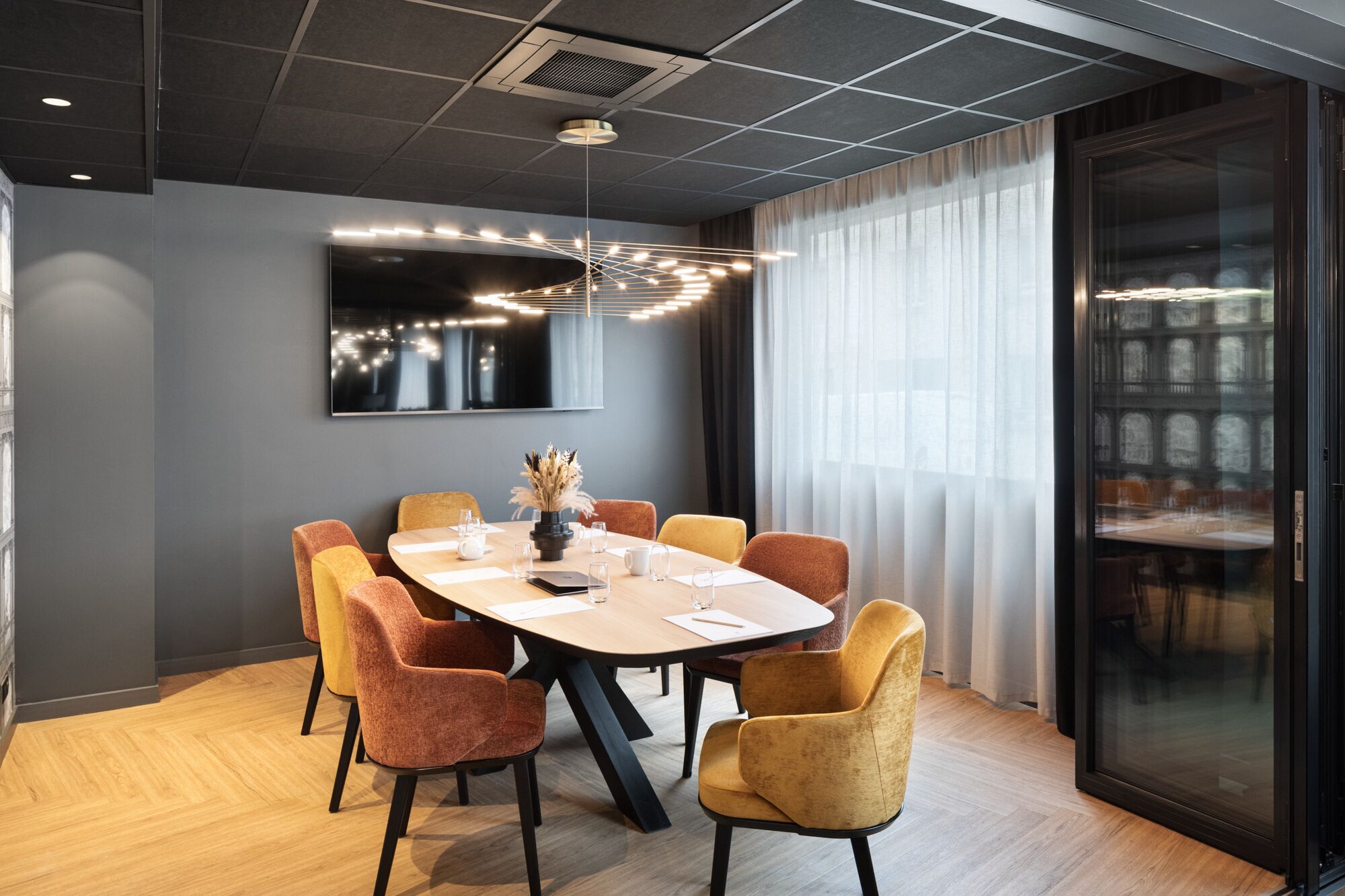 Een moderne vergaderruimte met een ronde tafel, zes stoelen en een groot raam met gordijnen.