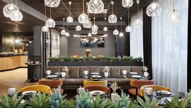 Un espace de restauration moderne avec plusieurs tables rondes, un coin salon central et des lustres en cristal suspendus.