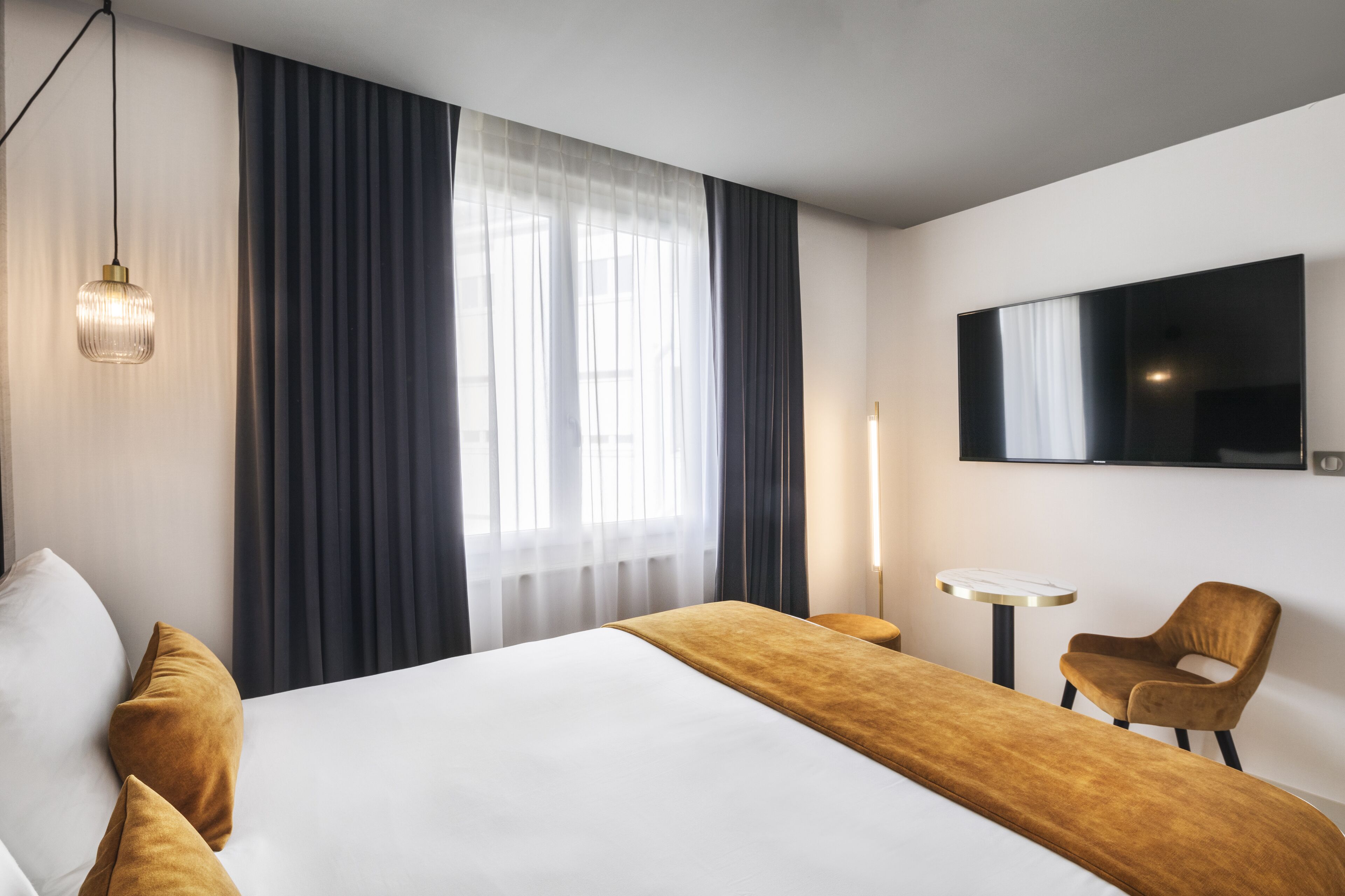 A hotel room with a large bed, a TV mounted on the wall, a small table, and a chair.