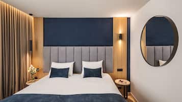 A modern hotel room with a large bed, a round mirror, and a wooden panel wall.