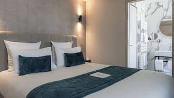 A modern hotel room with a large bed, a headboard with built-in lighting, a marble bathroom vanity, and a view of the bathroom through a door.
