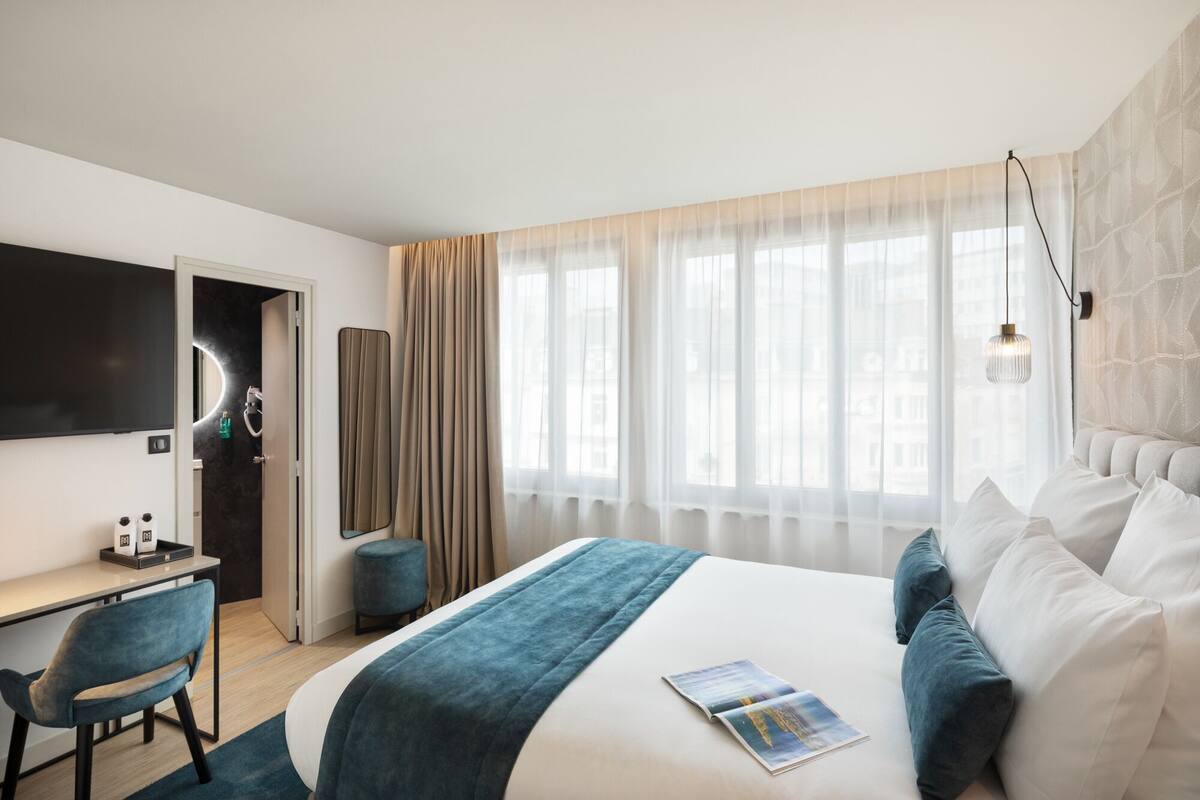 A modern hotel room with a bed, a desk, and a chair.