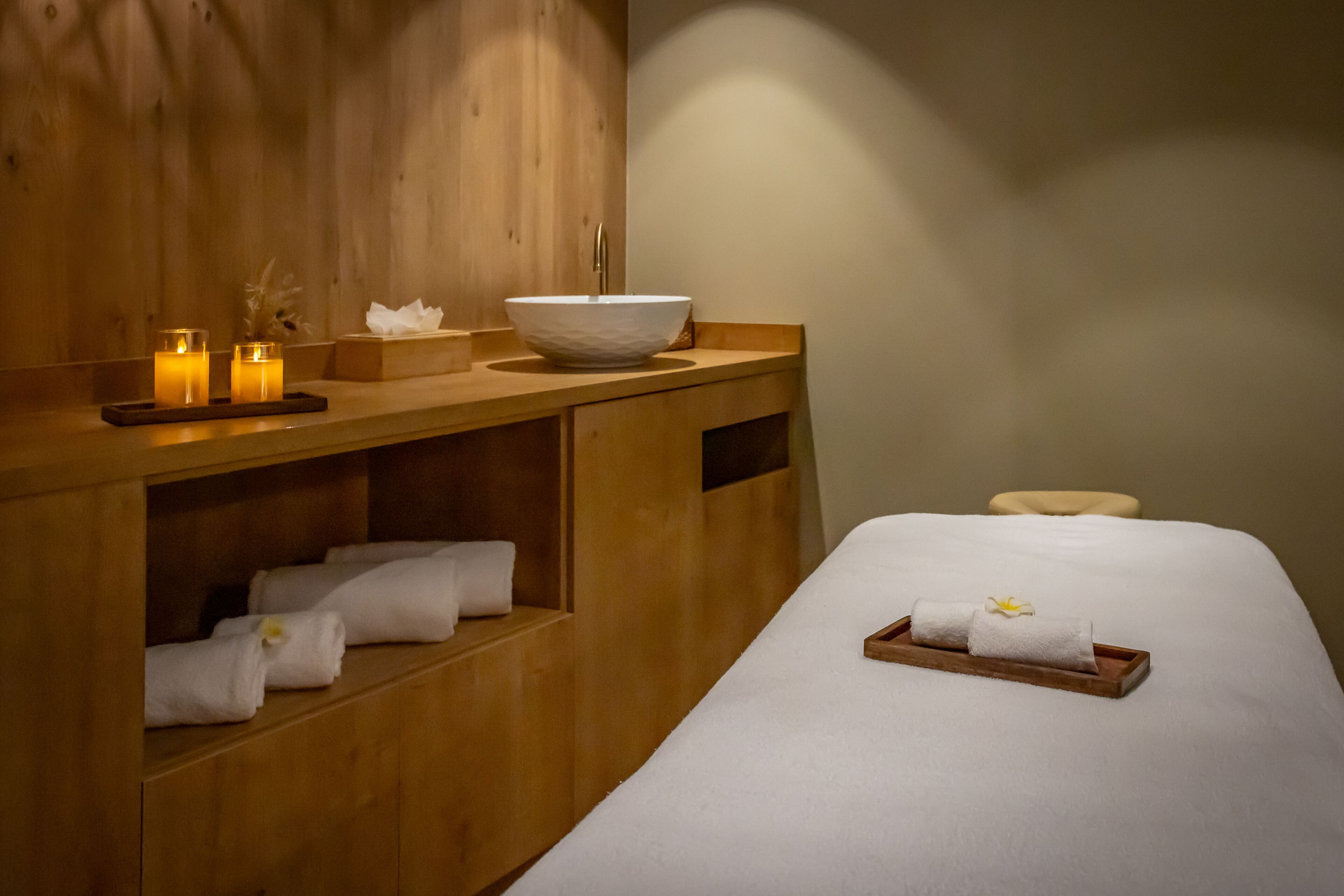 Un espacio de spa de madera con un lavamanos grande, velas y toallas dobladas con cuidado.