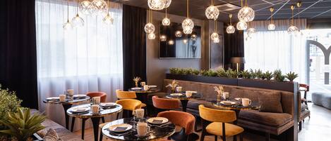 A modern dining area with round tables, cushioned seating, and pendant lighting.