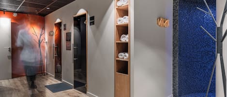 A hallway with a wooden shelf holding towels, a black door, and a blue mosaic wall.