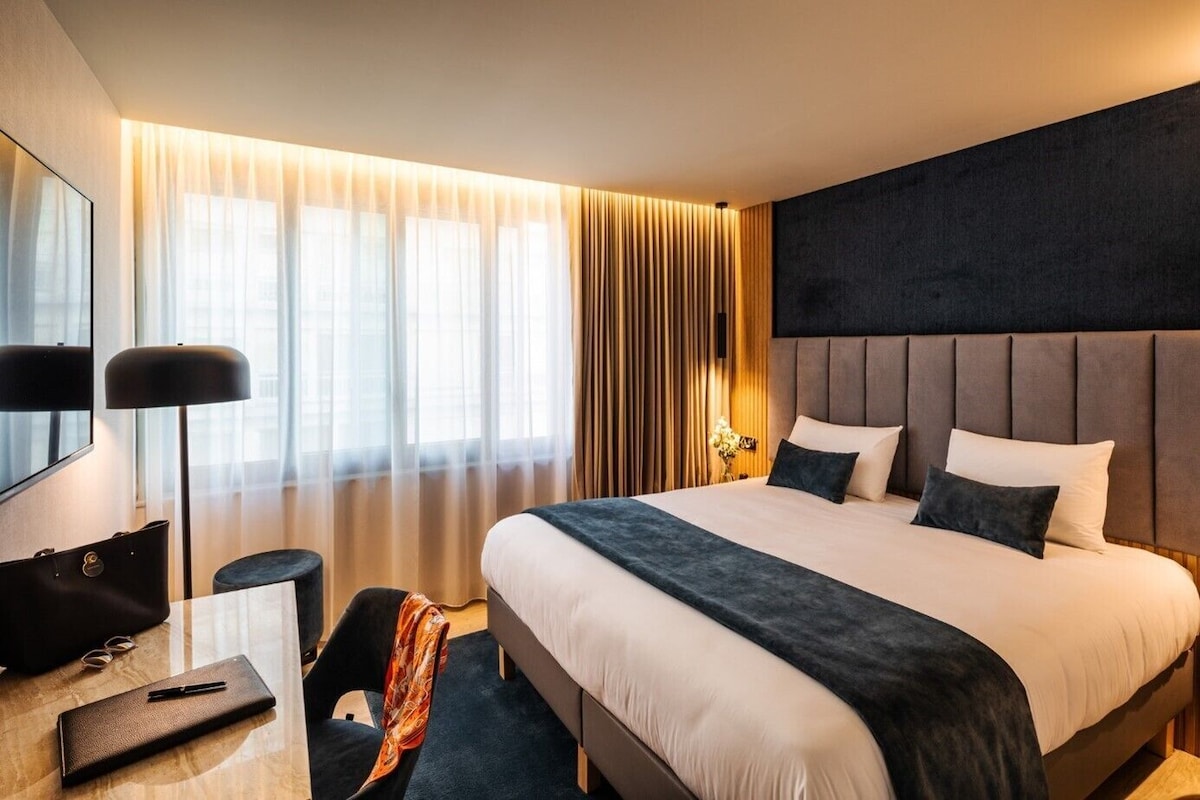 Una habitación de hotel con una cama grande, un escritorio con silla, una lámpara y un espejo.