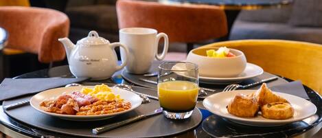 A breakfast table with plates of food, a teapot, a cup, and a glass of orange juice.