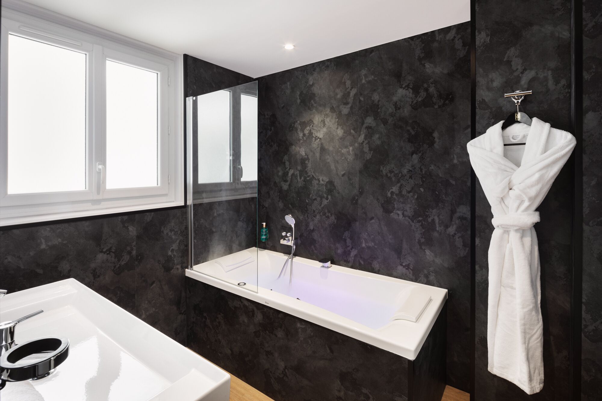 A modern bathroom with a freestanding bathtub, a large mirror, and a white robe hanging on a hook.