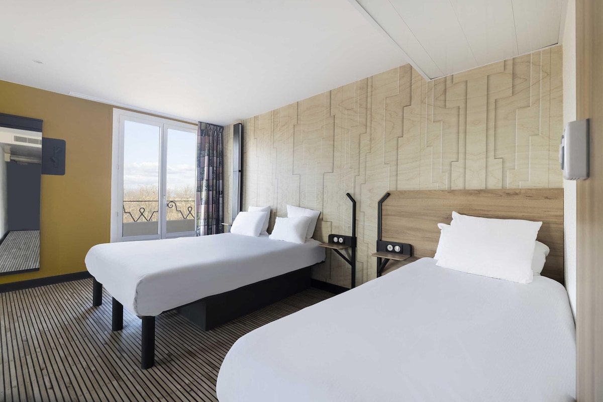 Ein Hotelzimmer mit zwei Betten, einem großen Fenster mit Blick und einer Holzvertäfelung.