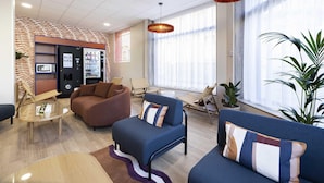 A modern lobby with seating, a vending machine, and large windows. - B&B HOTEL Perpignan Centre (Perpignan)