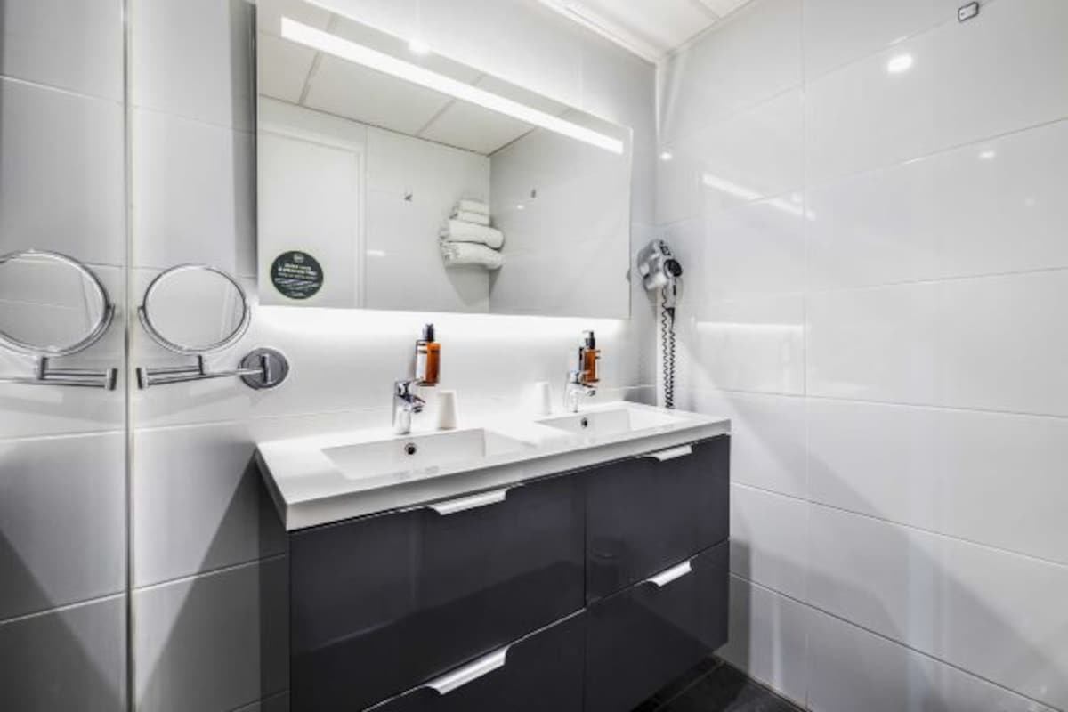 A modern bathroom with two sinks, a large mirror, and a hairdryer.
