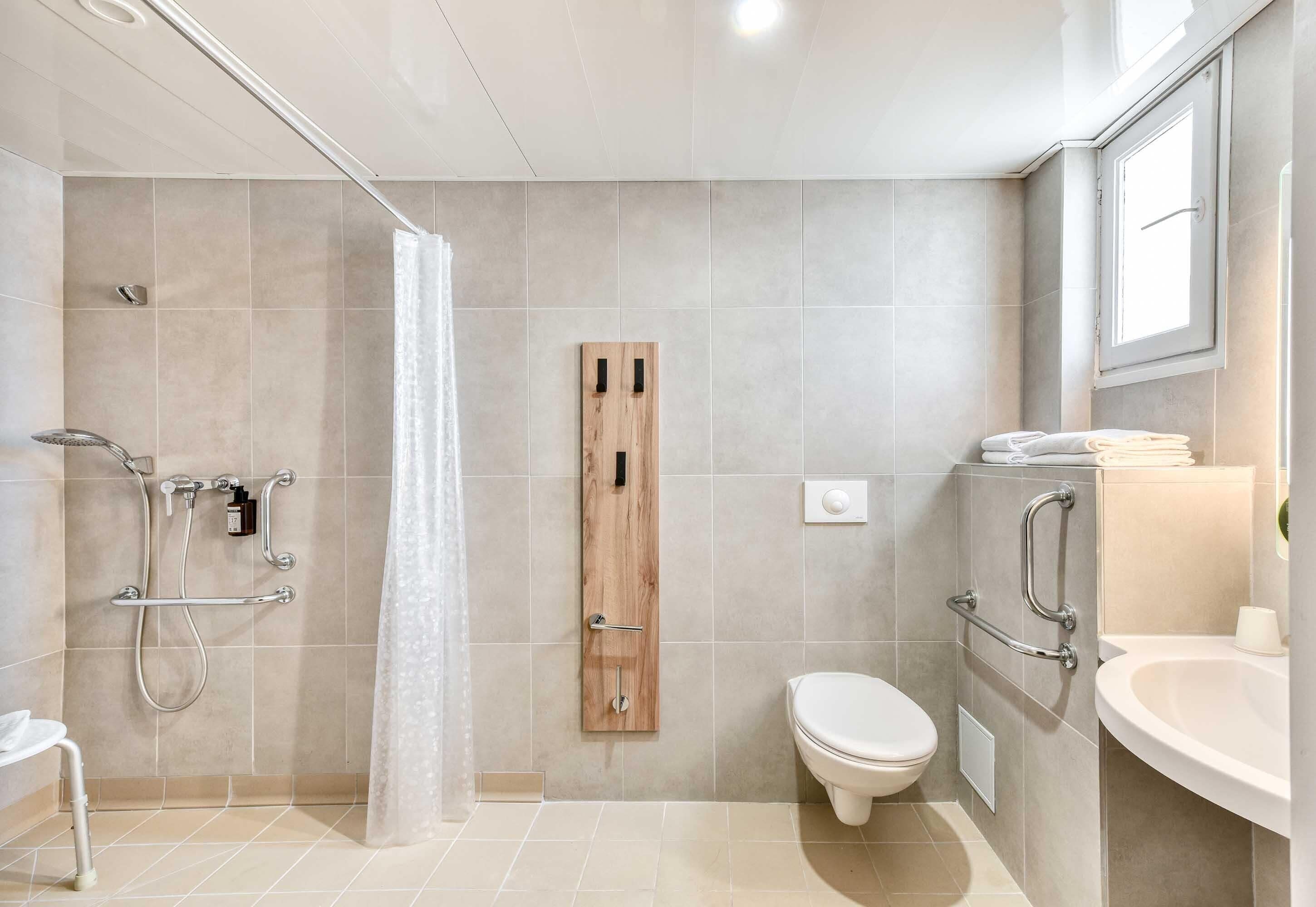 A modern bathroom with a shower, toilet, and sink, featuring a wooden accent panel and a glass shower curtain.