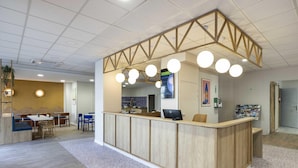 A reception area with a wooden counter, round hanging lights, a computer, and a bulletin board. - B&B HOTEL Perpignan Centre (Perpignan)