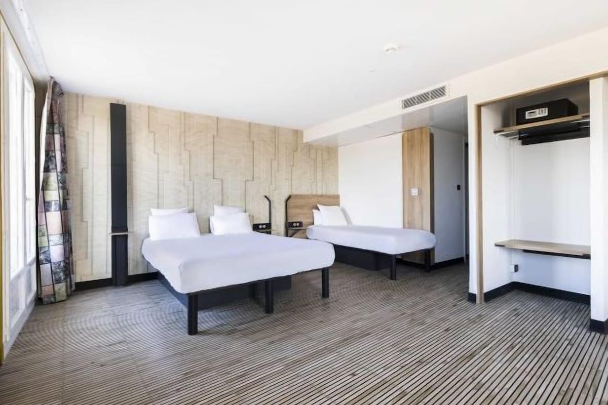Habitación de hotel con dos camas, un armario y una pequeña zona de estar.