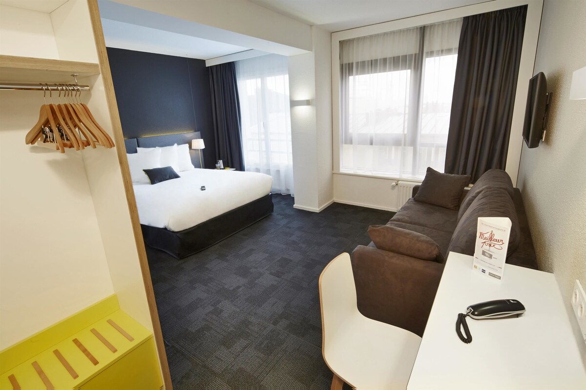A hotel room with a bed, a sofa, a table, and a TV.