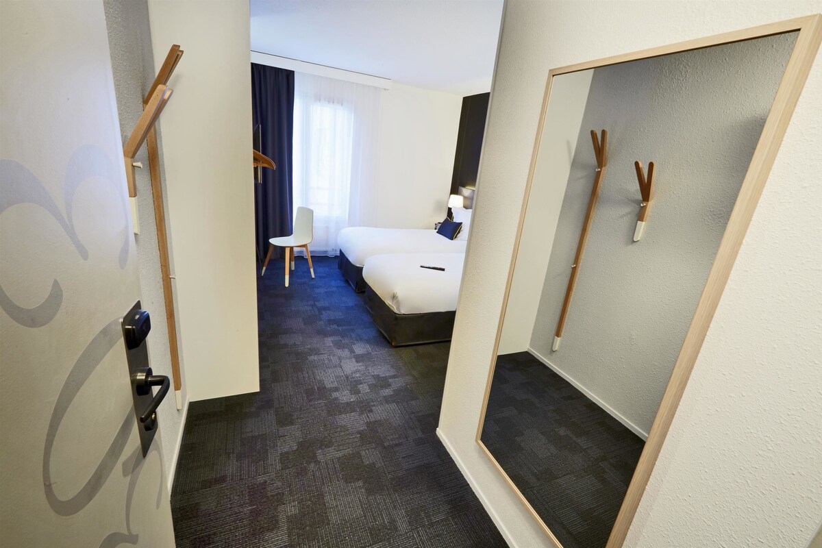 A hotel room with a bed, a chair, a desk, and a mirror.