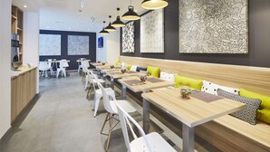 A modern restaurant with long communal tables, white chairs, and a wooden bench with green cushions. - Kyriad Brest Centre (Brest)