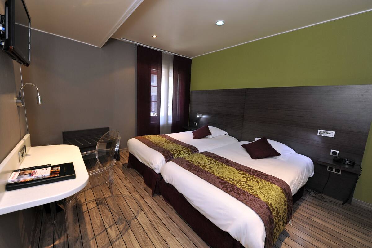 A hotel room with a large bed, a bedside table, a mirror, and a window with curtains.