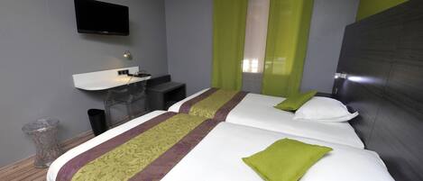 Habitación de hotel con dos camas, un escritorio, una silla, un televisor y una ventana con cortinas verdes.