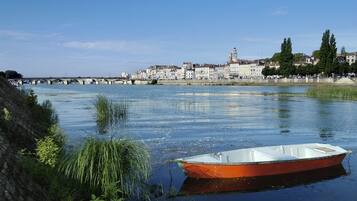 Une rivière avec un petit bateau, un pont et un paysage urbain en arrière-plan, avec des bâtiments et des arbres.