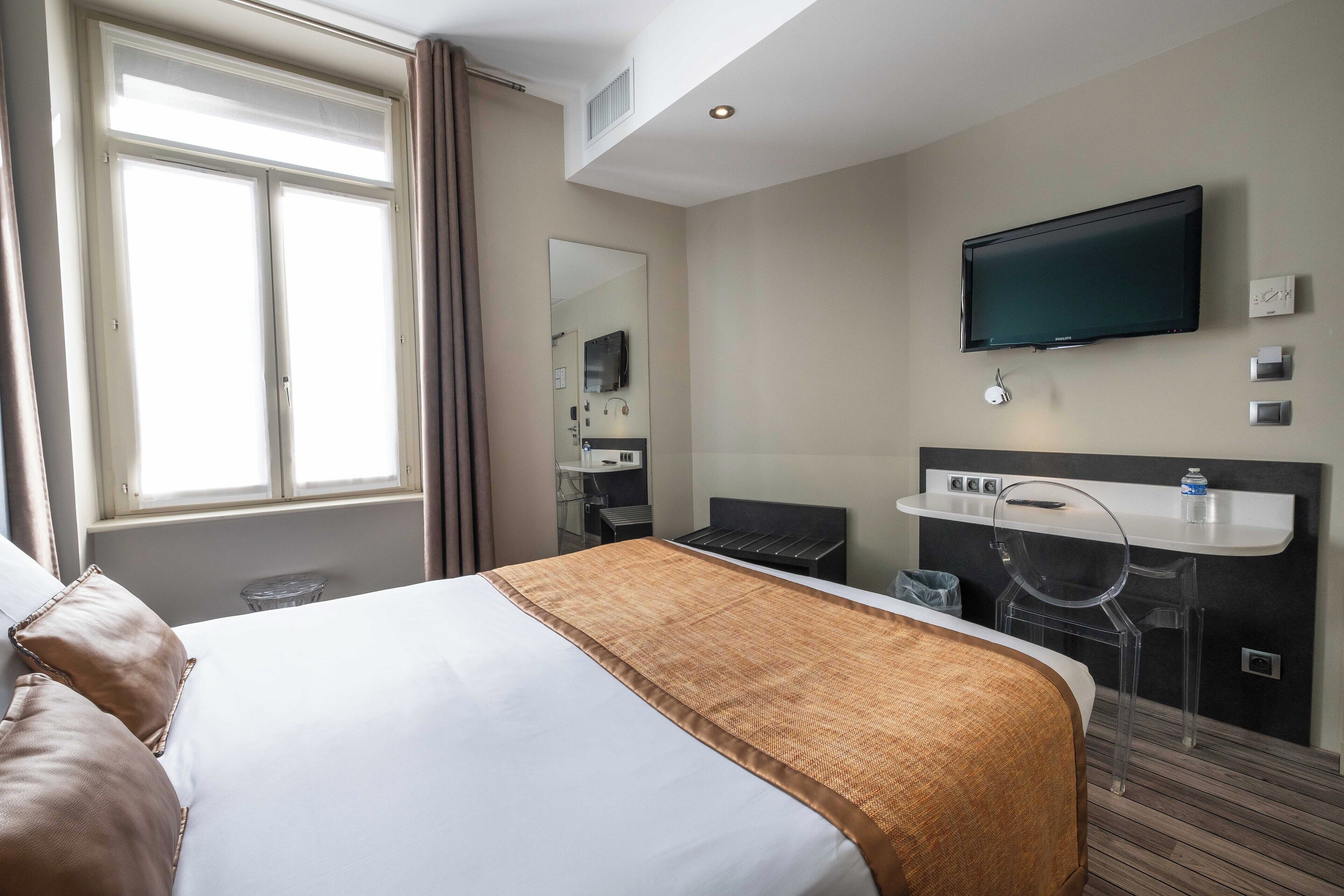 A hotel room with a large bed, a desk with a chair, a television, and a window with curtains.
