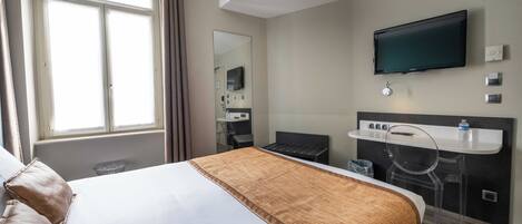 A hotel room with a large bed, a desk with a chair, a television, and a window with curtains.