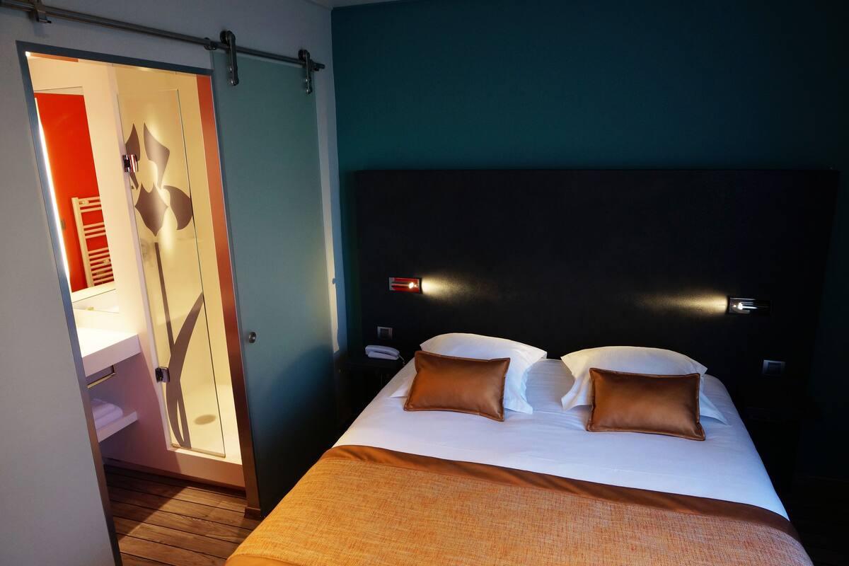 A hotel room with a bed, two pillows, a nightstand, a mirror, and a sliding door to a bathroom.