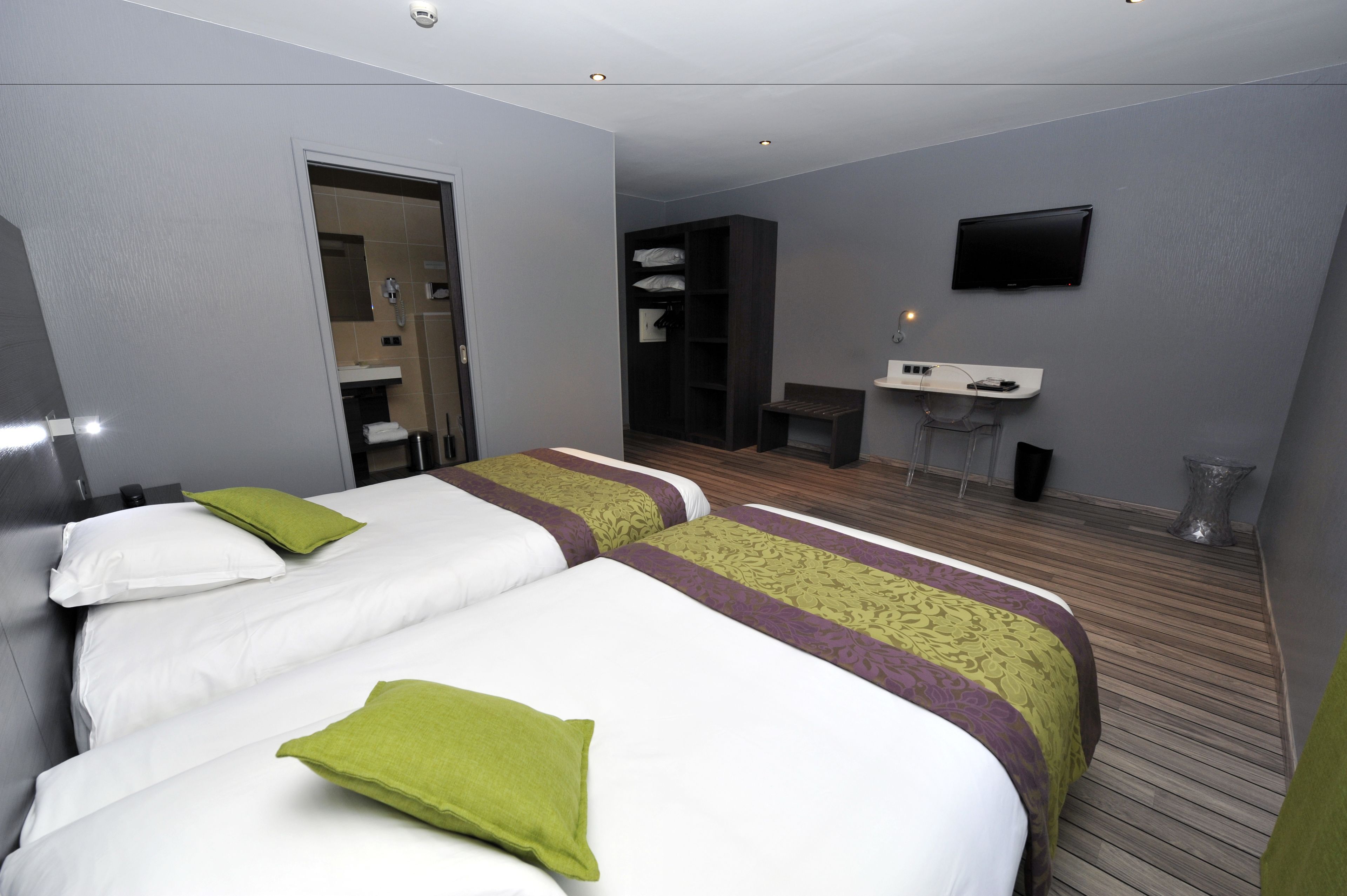A hotel room with two beds, a small desk, a TV, and a bathroom visible through an open door.